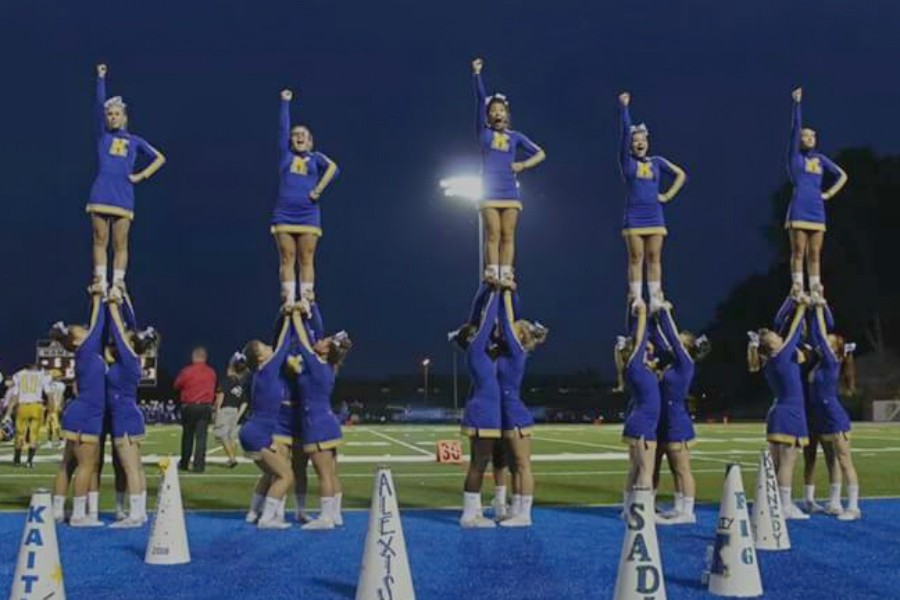 The fall cheerleading team hits a stunt while at a home football game. 