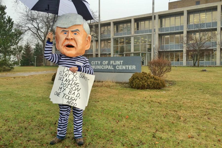 Mr. Bruce Fealk protests against the states handling of the Flint water crisis outside of Flints city hall Friday, Jan. 8, while wearing a papier-mâché  Rick Snyder head.