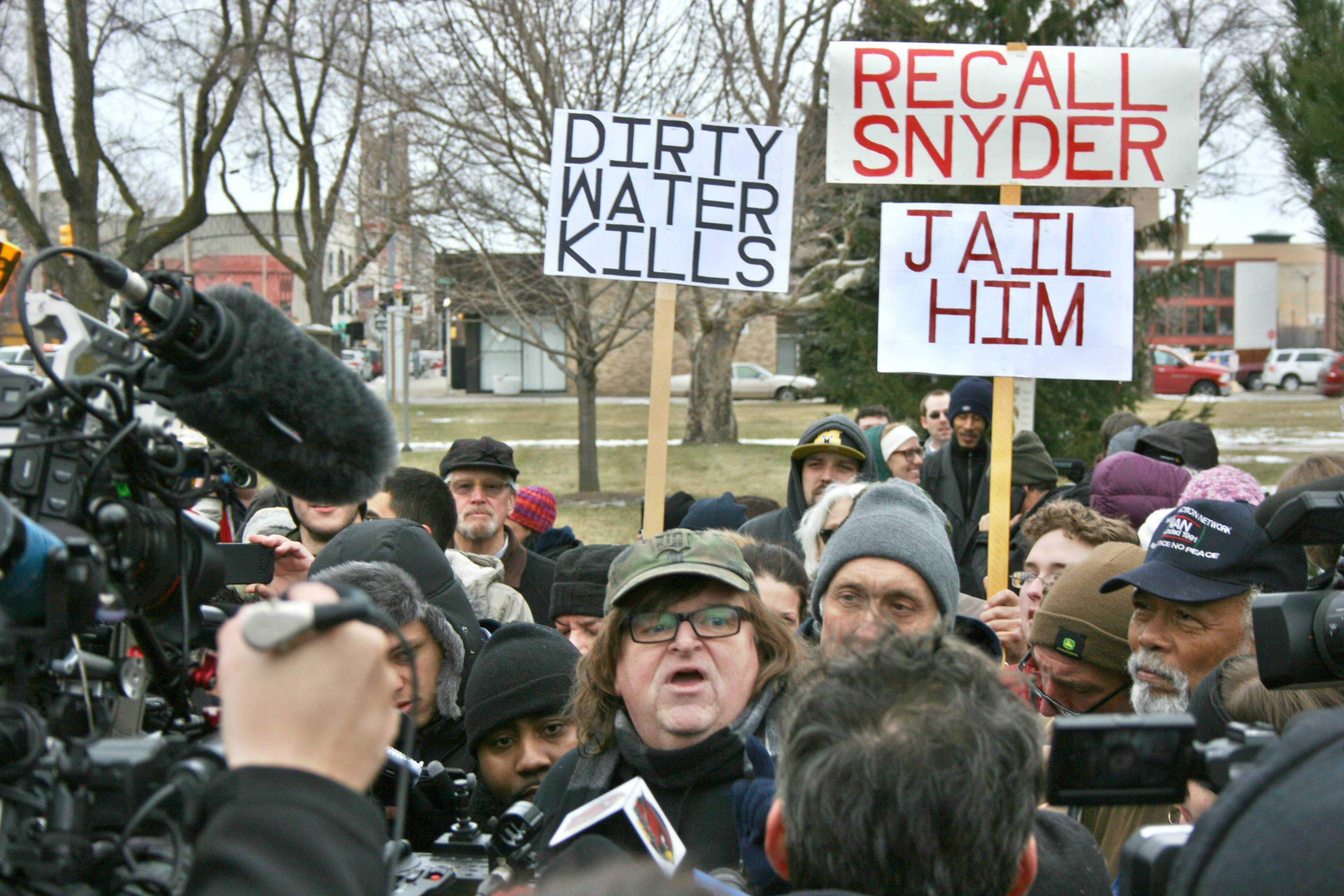 Protesters stand behind Mr. Michael Moore while he speaks to the press at Flint City Hall on Saturday, Jan. 16, about the Flint water problems.
