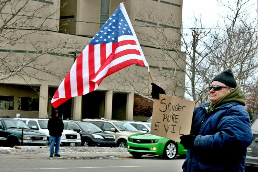 A protester holds a sign and waves the American flag on Saginaw Street outside of Flint City Hall on Saturday, Jan. 16, during a Flint water rally.