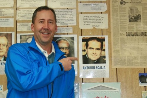 Mr. Andy Nester, political science teacher, points at a portrait of Associate Justice Antonin Scalia in his classroom.