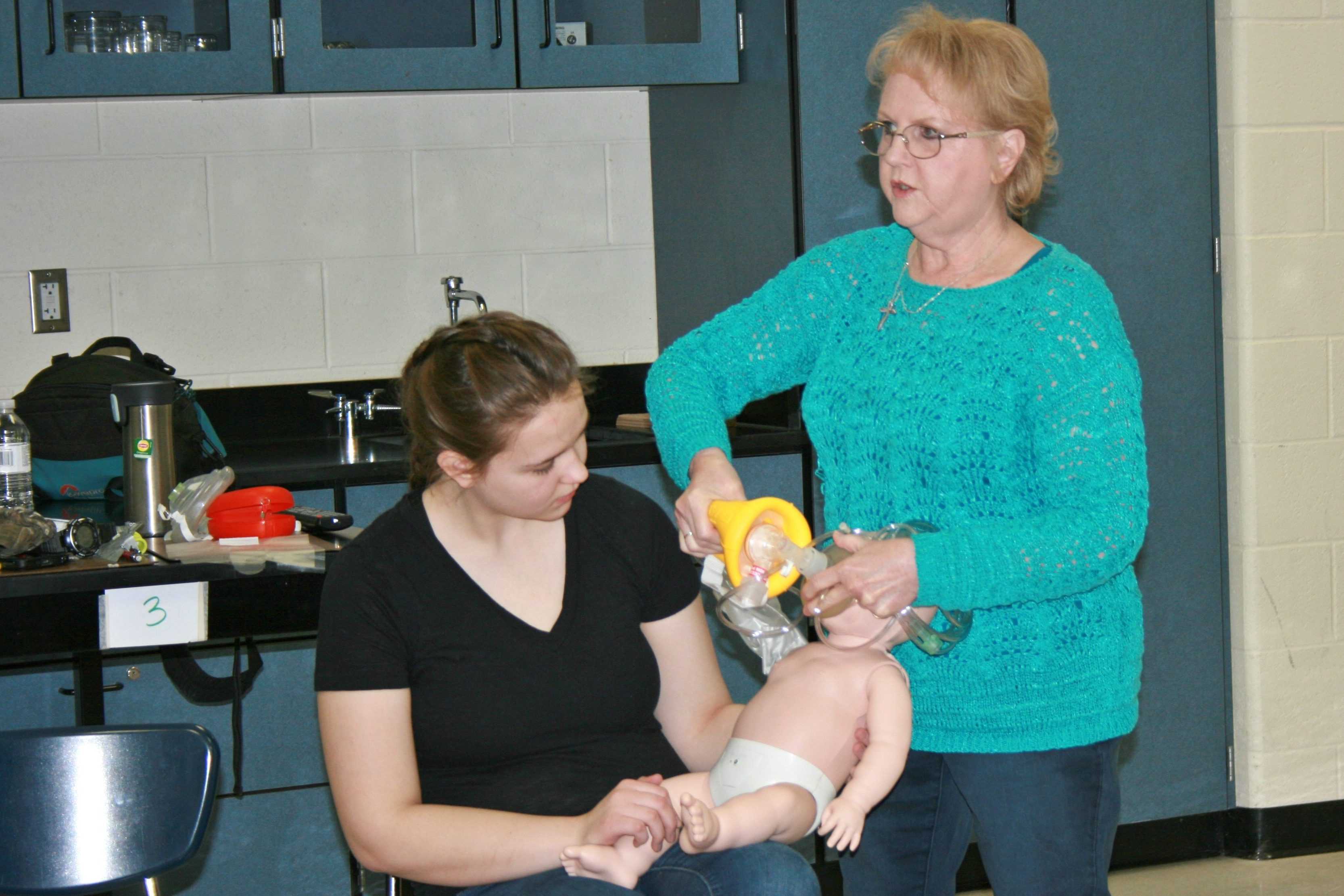 Senior Sarah Burns (sitting) is taught infant CPR by Ms. Dorie Mather, school nurse.