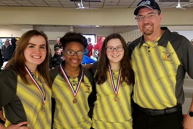 Junior Barbara Hawes (l to r), freshman Imari Blond, and sophomore Alexis Roof proudly stand with Coach Rob Ploof while wearing their Division 2 All-State medals.