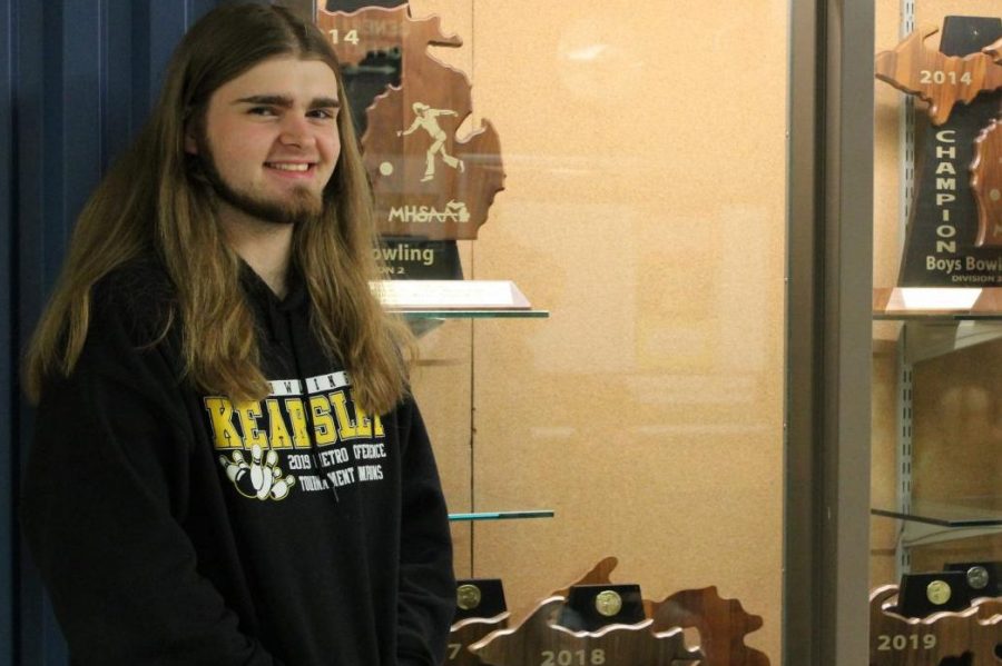 Senior Ethan Burke stands next to a cabinet holding the boys bowling teams MHSAA trophies. Burke is a key returner for the team this season.