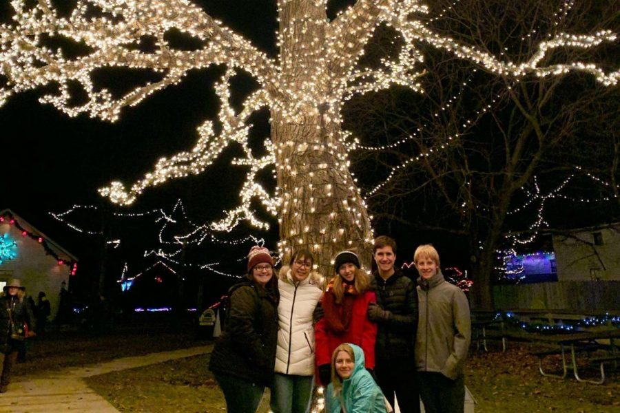 Sophomores Brooklyn Willhoite (l to r), Aizya Sorensen, Molly Gunn, Zoe Dustin, Jack Young, and Brodie Dustin huddle in front of a tree covered in lights at Christmas at Crossroads: Holiday Magic at Crossroads Village.