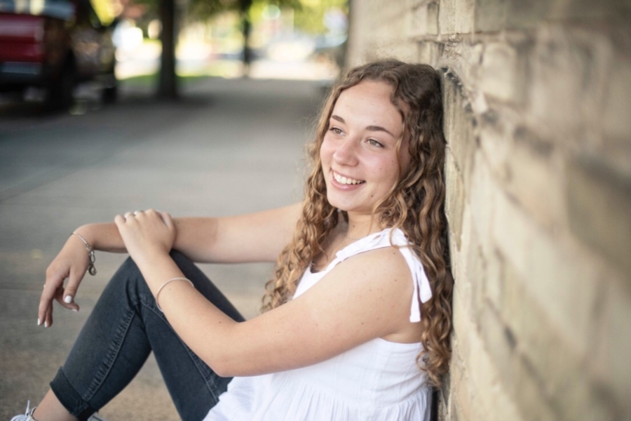 Senior+Mattalin+Bailey+leaning+against+a+brick+wall+with+a+smile.